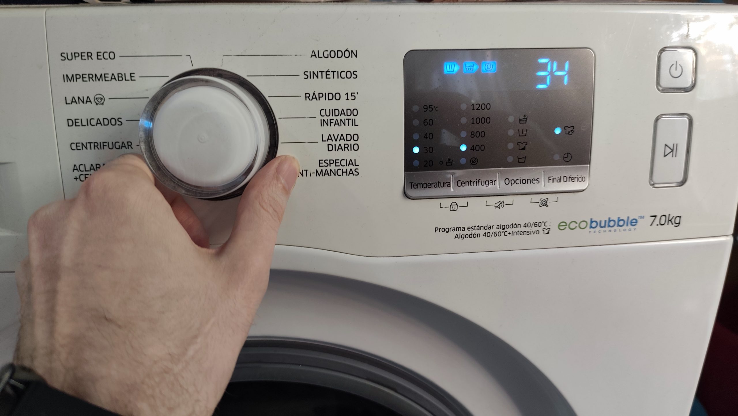 Hand turning washing machine dial to Delicados gentle setting with display showing 30 degrees and 400 RPM