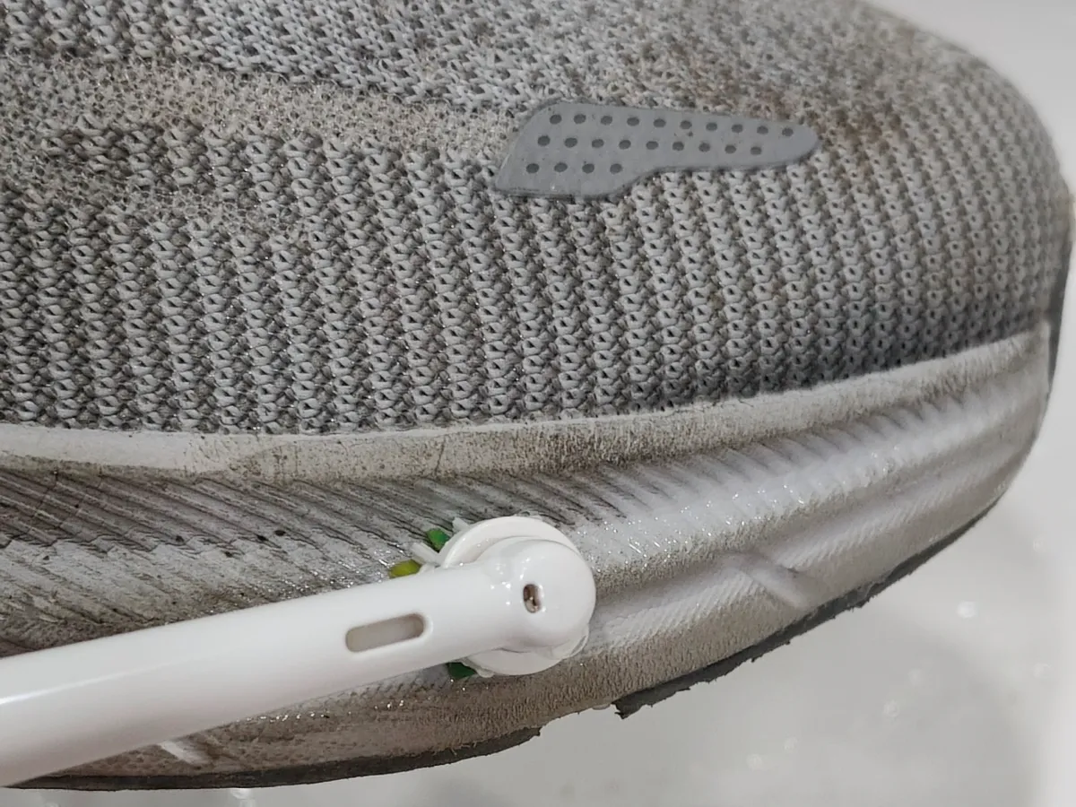 Electric toothbrush scrubbing the midsole edge of a grey sneaker over a bathroom sink