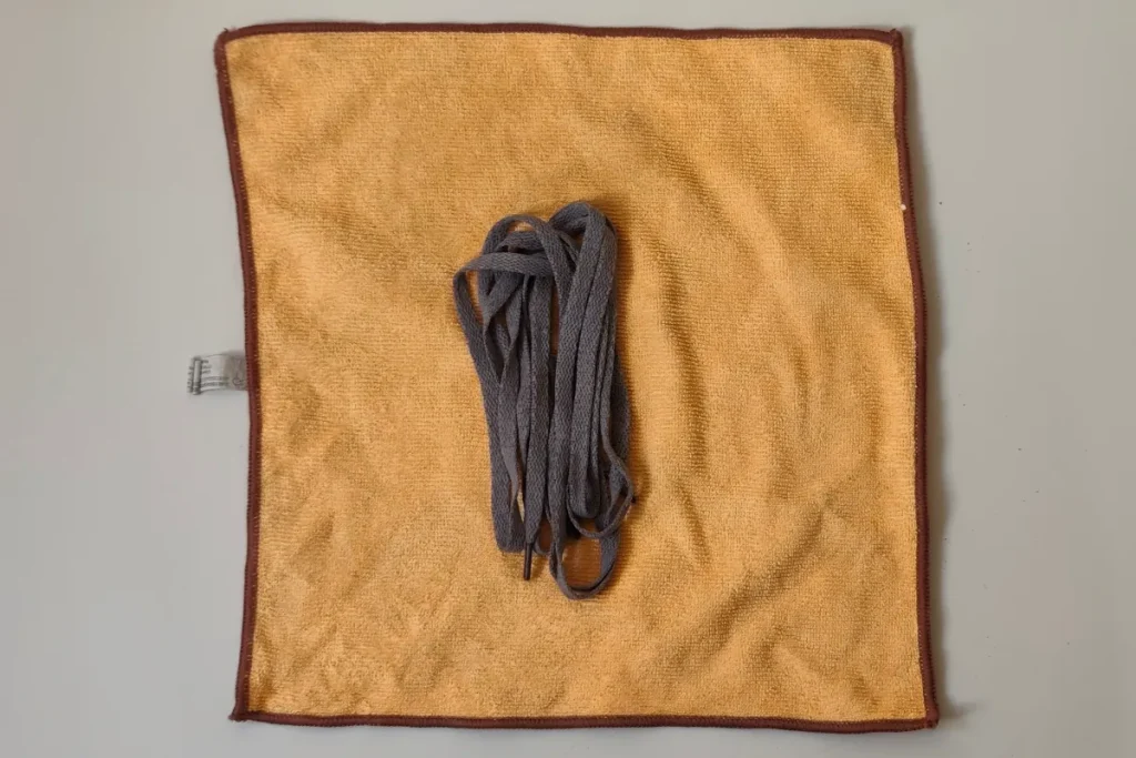Clean grey shoelaces laid flat on a yellow microfibre towel to air dry after hand washing