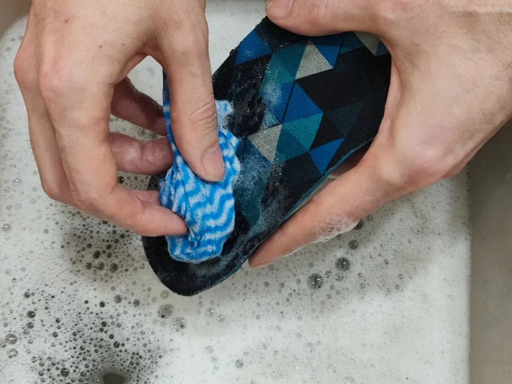 Hands cleaning blue patterned shoe insole with cloth in soapy water basin