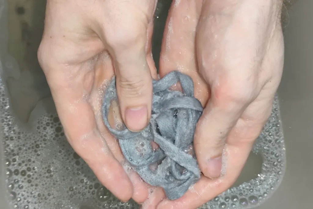 Hands washing grey shoelaces in soapy water basin squeezing and working through fingers